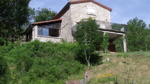 Una casa de piedra con balcón, rodeada de vegetación.