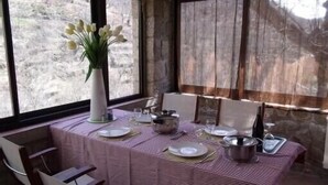 Una mesa de comedor preparada con platos, cubiertos y un florero, con vistas a un paisaje rocoso a través de amplios ventanales.