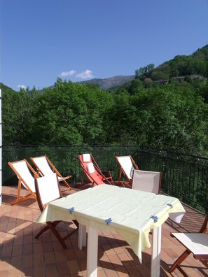 Um terraço com mesa e cadeiras, cercado por um muro verde e árvores.