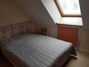 Una habitación pequeña con techo inclinado, una cama individual, un respiradero y una ventana.