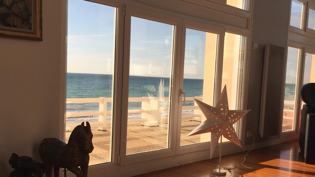 Quarto com grandes janelas com vista para a praia, piso de madeira e decoração estrelada.