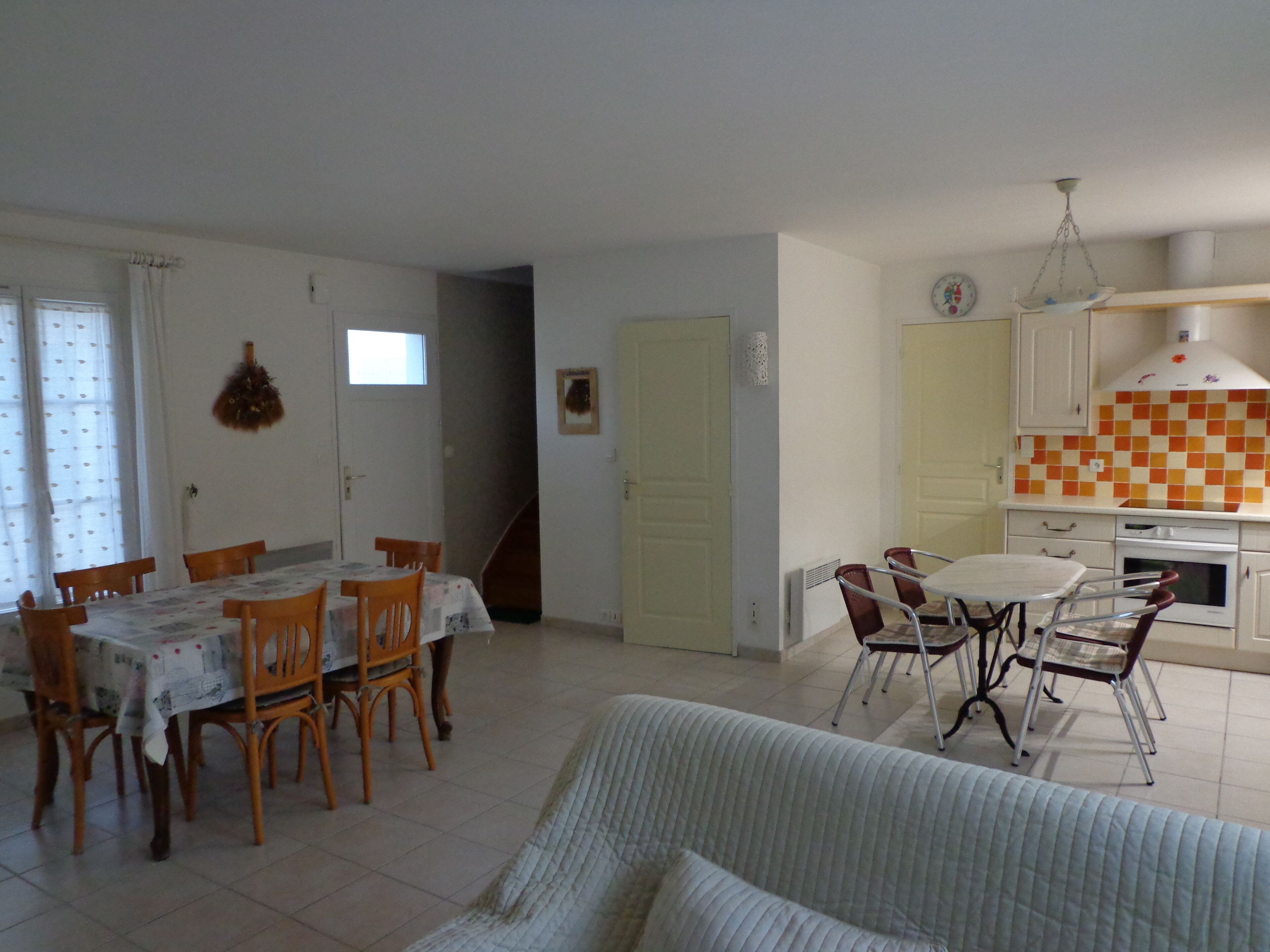 A dining area with a table and chairs, a kitchen with a checkered backsplash, and a living area with a sofa.