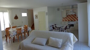 A living room with a sofa, dining table, chairs, and a kitchen area with cabinets and a stove. - Pretty house classified 3 *** style retais (Saint-Martin-De-Ré)