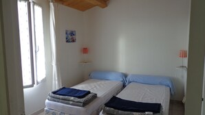 A room with two beds, a window with curtains, a small table with a lamp, and a painting on the wall. - Pretty house classified 3 *** style retais (Saint-Martin-De-Ré)