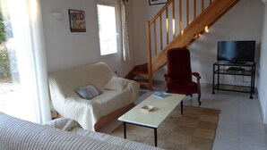A living room with a sofa, a red chair, a small table, a TV on a stand, and a staircase. - Pretty house classified 3 *** style retais (Saint-Martin-De-Ré)