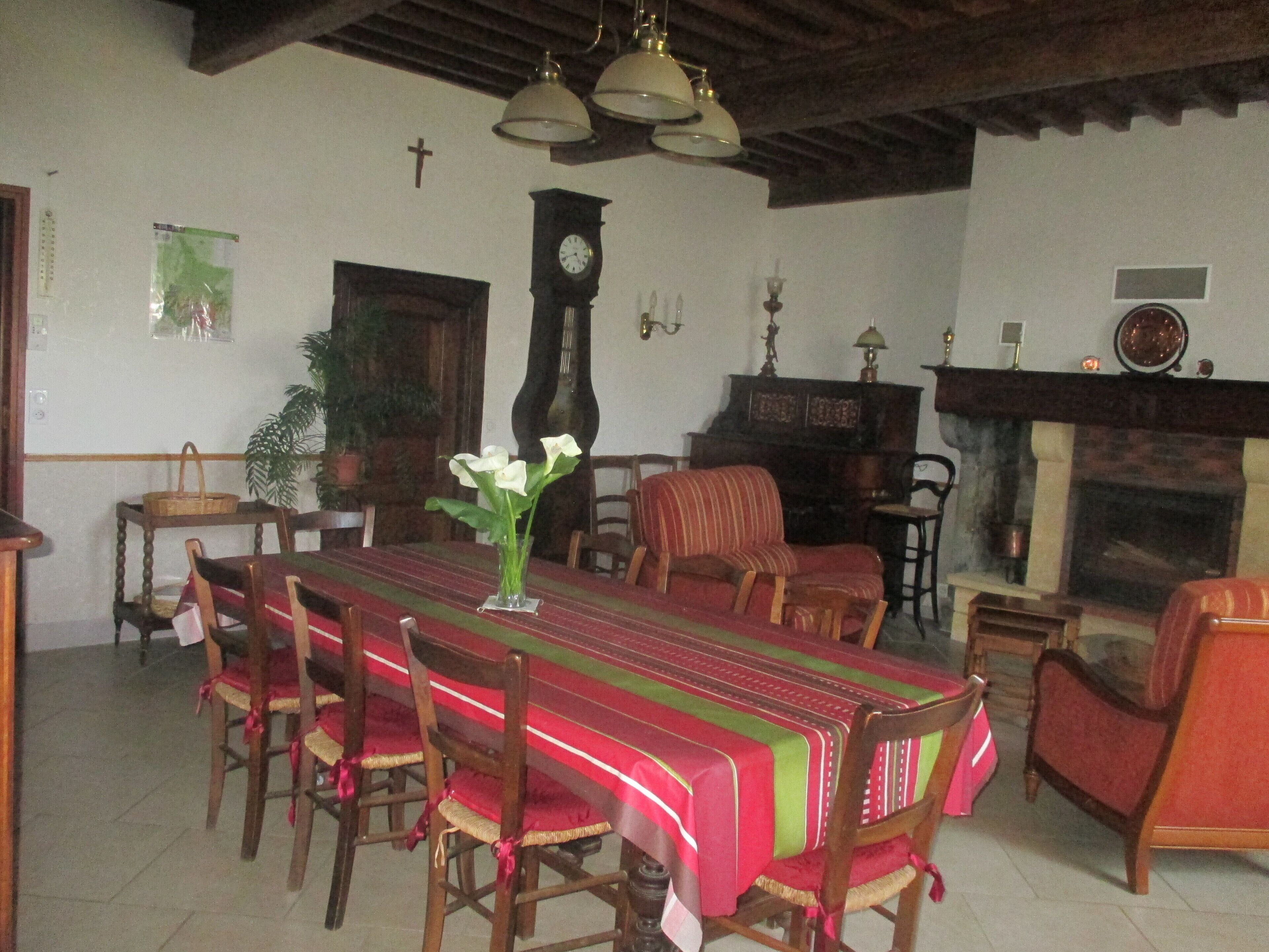 A dining area with a long table, chairs, a clock, and a fireplace.