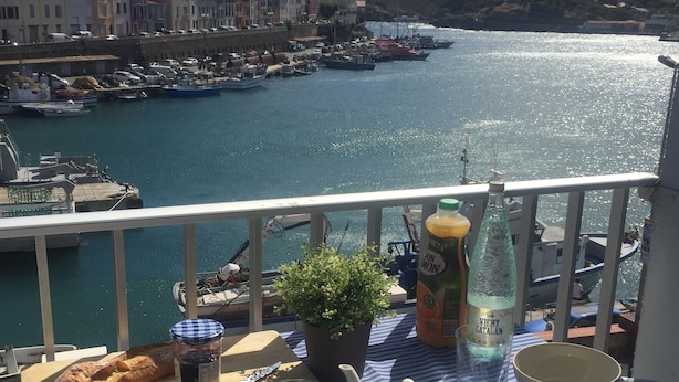Un balcón con una mesa dispuesta para el desayuno, con vistas a un puerto con barcos y edificios.