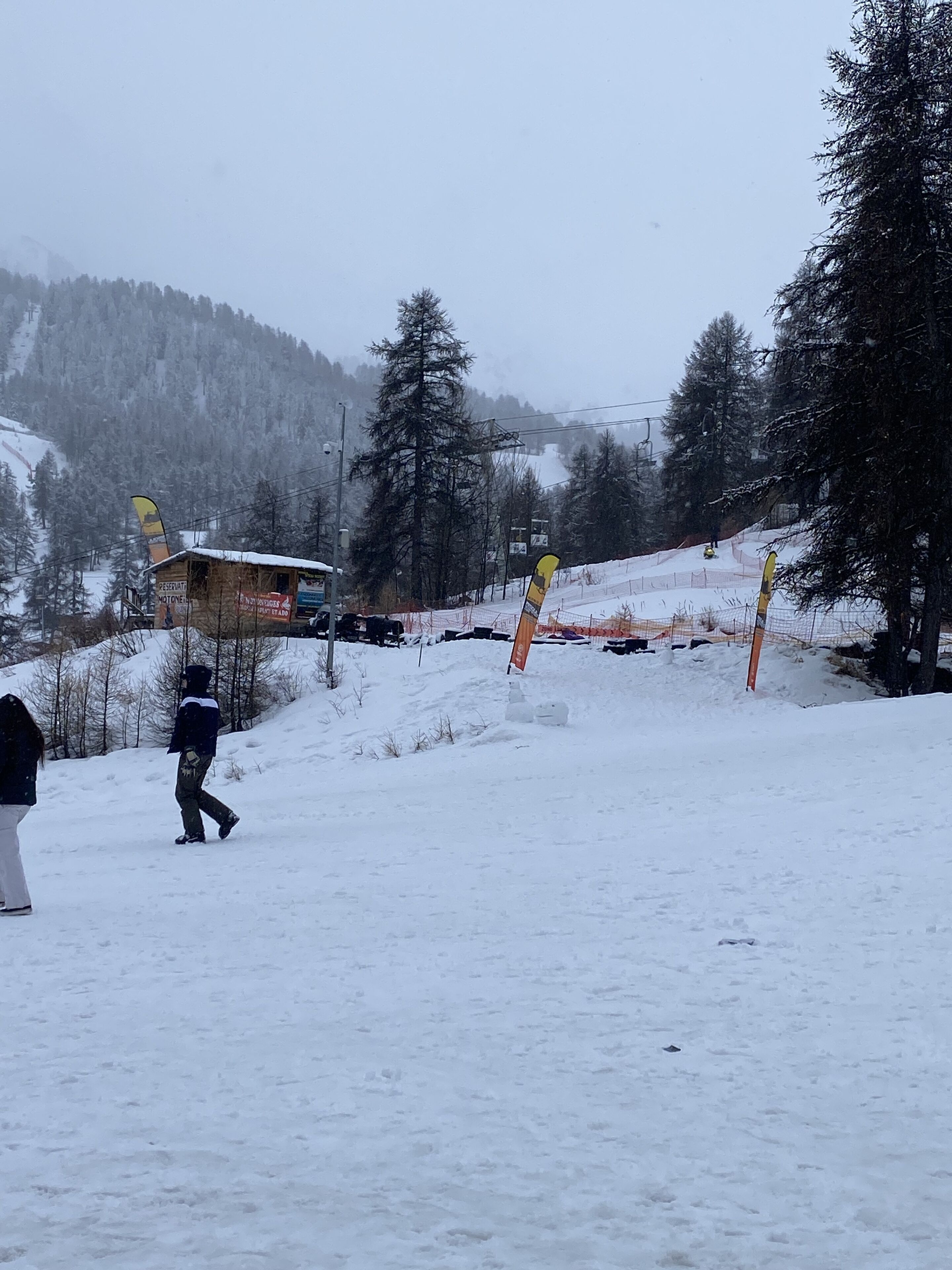 A snowy landscape with a ski lift, a wooden shelter, and a person walking.