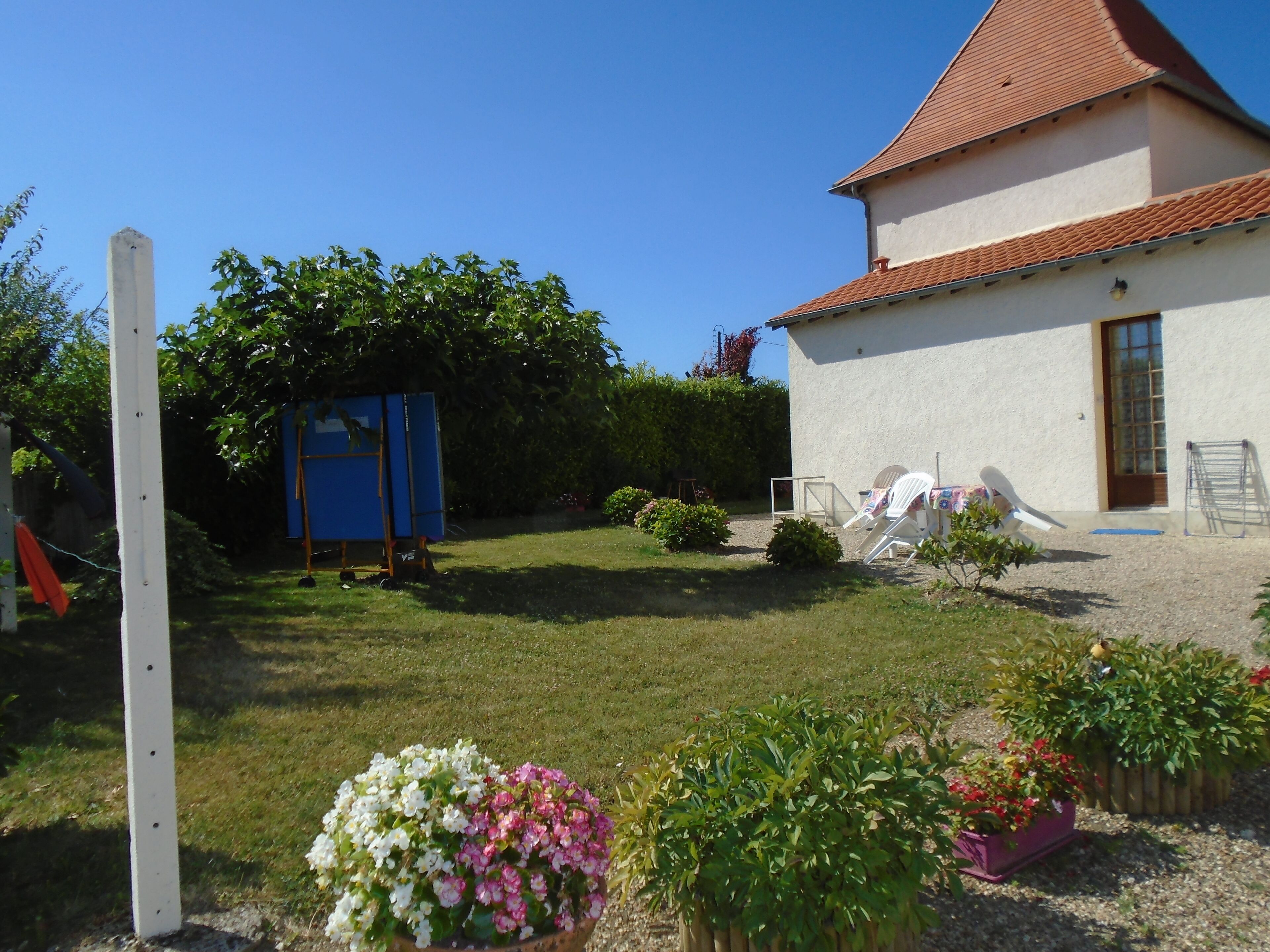 A house with a white exterior and a red roof, a small garden with potted plants, and outdoor furniture.