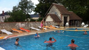 Une piscine avec des personnes dans l’eau, des chaises longues et un bâtiment en arrière-plan.