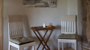 Une pièce avec deux chaises blanches, une petite table en bois et un tableau encadré représentant un paysage, accroché au mur.