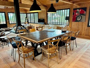 A spacious dining area with a large wooden table and chairs, surrounded by wooden walls and large windows. - Large charming cabin (Lège-Cap-Ferret)