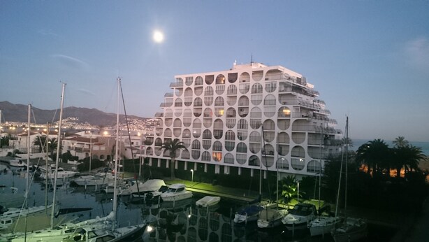 Un hôtel à plusieurs étages doté d’une architecture originale, avec des fenêtres circulaires, situé près d’une marina où sont amarrés des bateaux.
