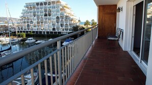 Un balcon offrant une vue sur un port de plaisance et un bâtiment remarquable avec des fenêtres rondes.