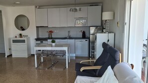 Une cuisine moderne avec des meubles blancs, un coin repas avec une table et des chaises, et un canapé dans l’espace salon.