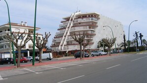 Un hôtel à plusieurs étages doté de balcons, d’un parking et situé dans une rue bordée d’arbres et où circulent des voitures.