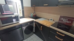 Een compacte keuken met een magnetron, vaatwasser en wasmachine. Er is een houten aanrecht, een spoelbak en een kastje met het opschrift 'MIAM MIAM'.