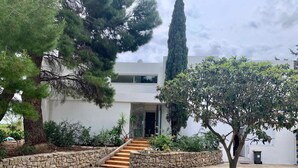 A modern two-story building with a stone wall and a wooden staircase leading to the entrance. - The Zen villa, sun and idleness (Pinet)