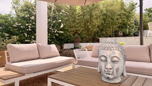 An outdoor seating area with a beige sofa, a wooden table, and a Buddha statue. - The Zen villa, sun and idleness (Pinet)