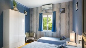 Een slaapkamer met twee bedden, een witte kast, een raam met gordijnen, een stoel en een bedlampje.