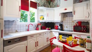 Een keuken met witte kastjes, een rode spoelbak en een eethoek met een tafel en stoelen.