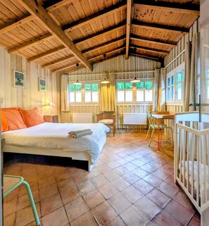 A rustic wooden room with a bed, a table, chairs, and a crib.