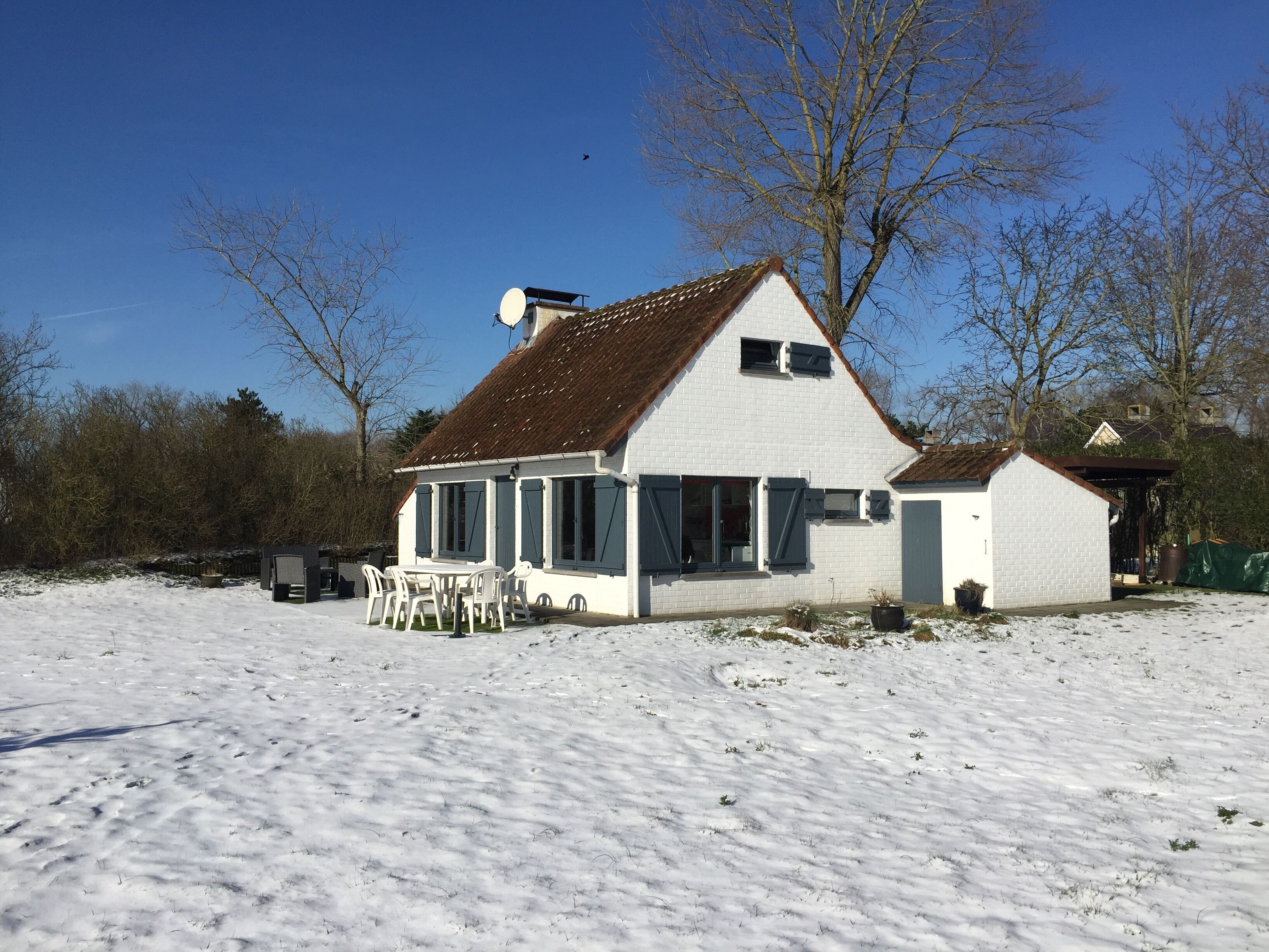 A white house with a brown roof, a satellite dish, and a small porch with chairs.