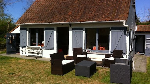 Une maison avec un toit en tuiles, une véranda meublée de meubles en osier et un banc.