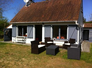 Une maison avec un toit en tuiles, une véranda meublée de meubles en osier et un banc.