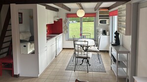 Une cuisine compacte avec des meubles blancs, un plan de travail rouge et un coin repas comprenant une table et des chaises.