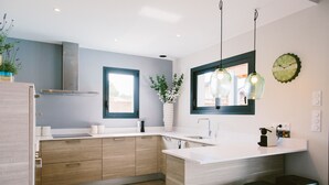 A modern kitchen with wooden cabinets, a white countertop, a built-in stove, and a window with a view. - Architect-designed villa between town center and beach - Heated pool (Capbreton)