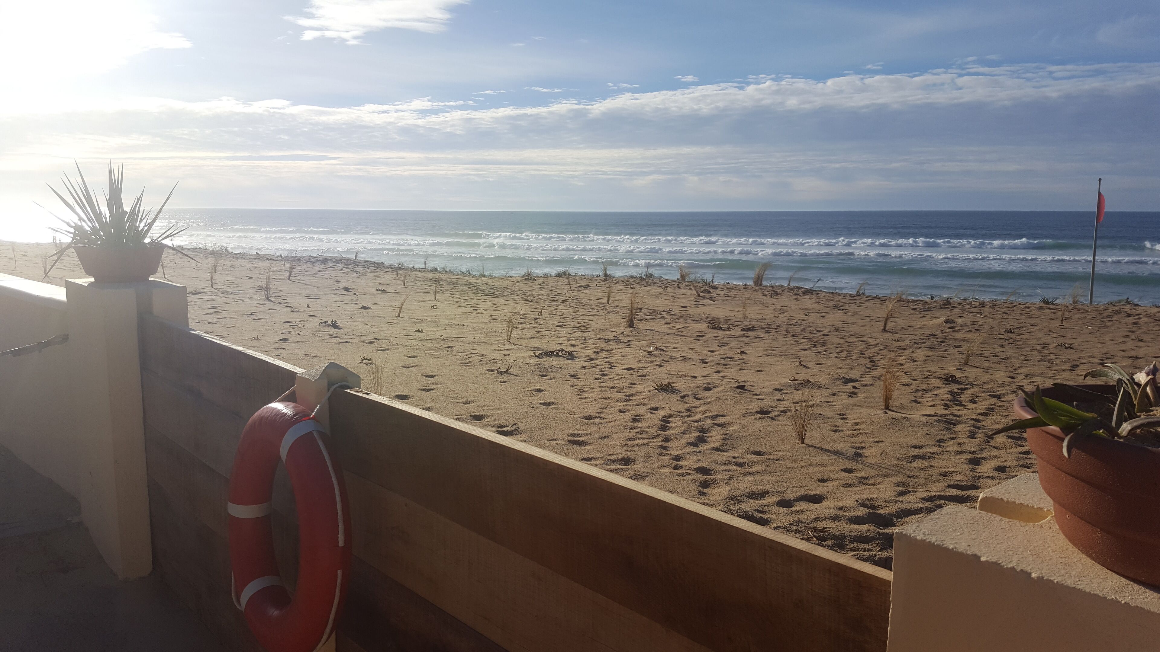 Blick auf einen Strand vom Balkon aus, mit einem Rettungsring und Blumentöpfen.