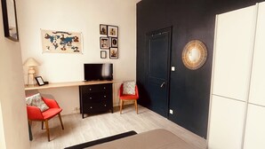 A bedroom with a bed, a desk, two chairs, a TV, and a door.