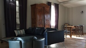 A living room with a black leather sofa, a wooden cabinet, and a dining area with chairs and a table. - Provencal house in a quiet and in the heart of the village of Gigondas (Gigondas)