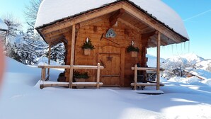 A wooden cabin with a snow-covered roof, wooden porch, and potted plants. - Apartment in the owner's chalet in CREST-VOLAND (COHENNOZ)