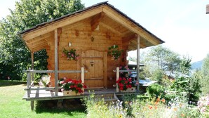 A wooden cabin with a porch, surrounded by a garden with various flowers and plants. - Apartment in the owner's chalet in CREST-VOLAND (COHENNOZ)
