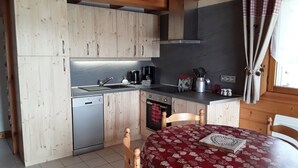 A compact kitchen with wooden cabinets, a sink, a coffee maker, and a dining table with a patterned tablecloth. - Apartment in the owner's chalet in CREST-VOLAND (COHENNOZ)
