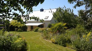 A residential property with a well-maintained lawn, a variety of flowering plants, and a house with a sloped roof and solar panels. - Between Saint-malo and Cancale, ideal for families or friends, 2 kms from the beach (Saint-Coulomb)