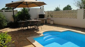 En baghave med swimmingpool, grillområde og spisebord med stole.