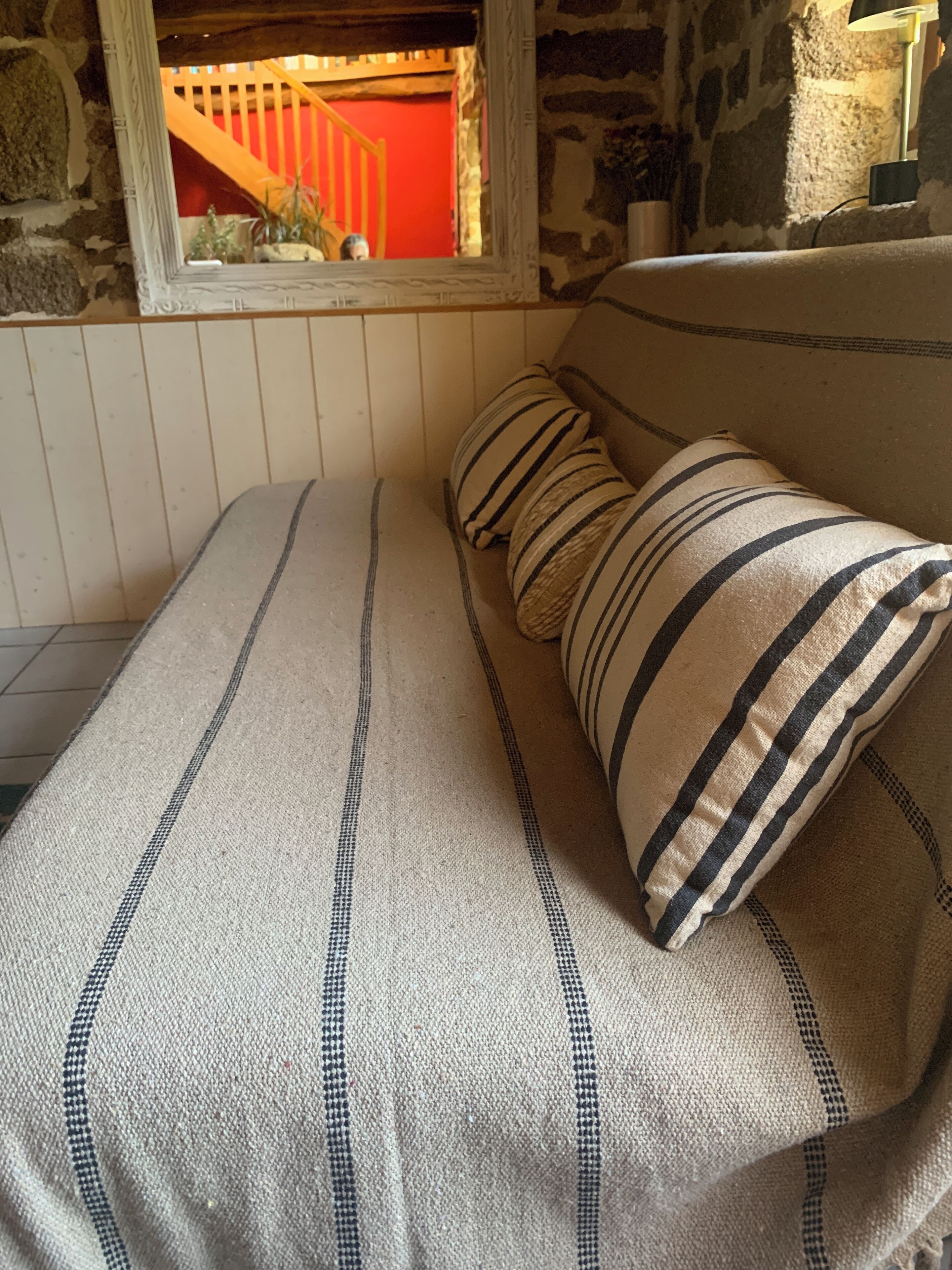 A bed with striped pillows and a plain bedspread, a stone wall, and a wooden staircase in the background.