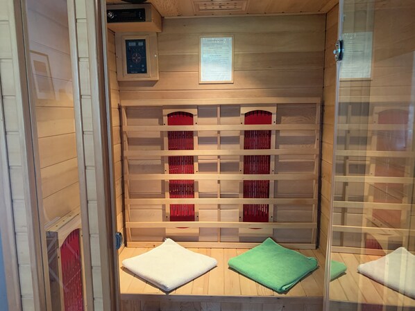 A sauna room with wooden benches, a control panel, and a glass partition.