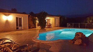 En swimmingpool med jacuzzi, omgivet af en terrasse med stole og et bord.