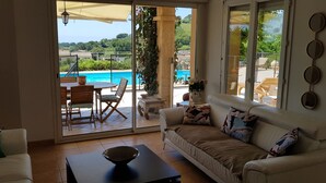 Et værelse med sofa, bord og udsigt til swimmingpool samt udendørs møbler.