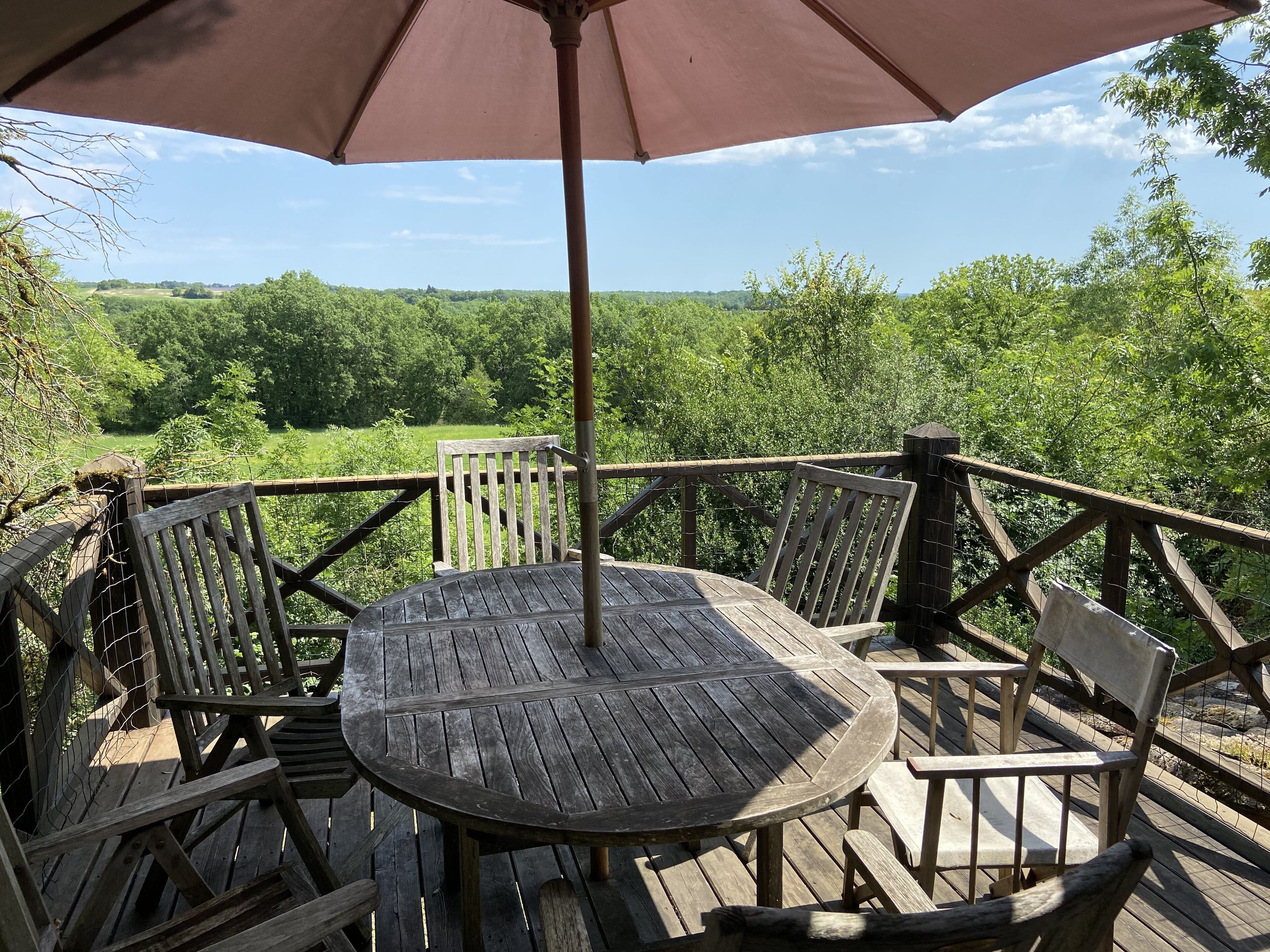 Eine Holzterrasse mit Tisch und Stühlen, umgeben von einem Hollerdacht, mit Blick auf eine üppige, grüne Landschaft.