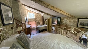 A bedroom with a large bed, a wooden wardrobe, a stone wall, and a bathroom with a bathtub. - Beautiful Authentic Stone House In The Lot REDUCED RATE ! (Montcuq-En-Quercy-Blanc)