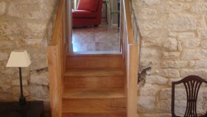 A wooden staircase leading to a living room with a stone wall, a red sofa, and a framed picture on the wall. - Beautiful Authentic Stone House In The Lot REDUCED RATE ! (Montcuq-En-Quercy-Blanc)