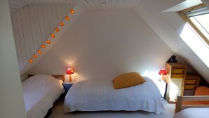 A cozy attic bedroom with two beds, a checkered rug, and a sloped ceiling with string lights.