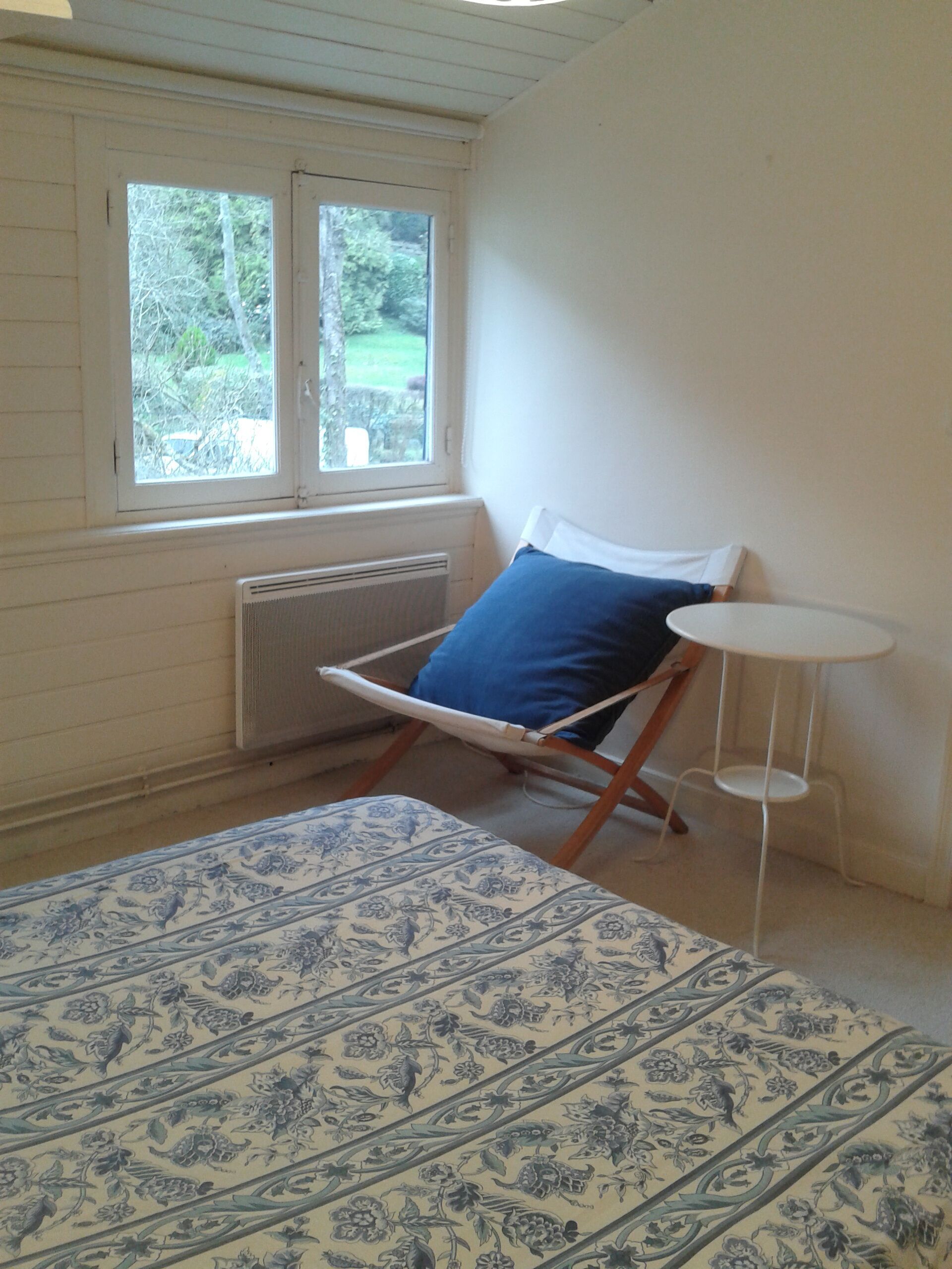 A room with a bed, a chair, a small table, and a window with a view of trees.