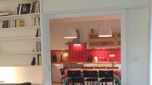 A modern living room with a grey sofa, a bookshelf, and a kitchen in the background.