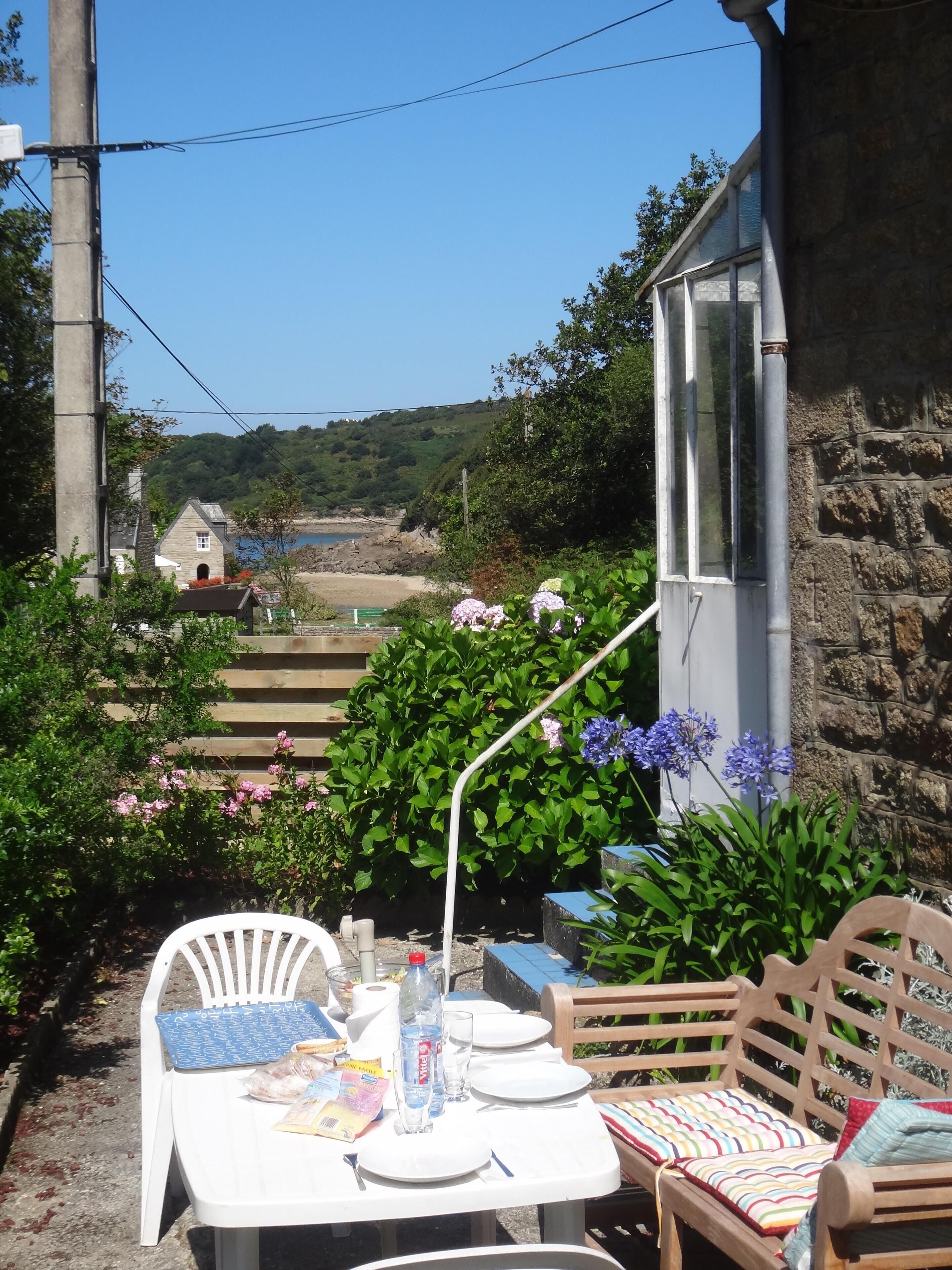 An outdoor dining area with a table set for two, surrounded by greenery and a stone wall.